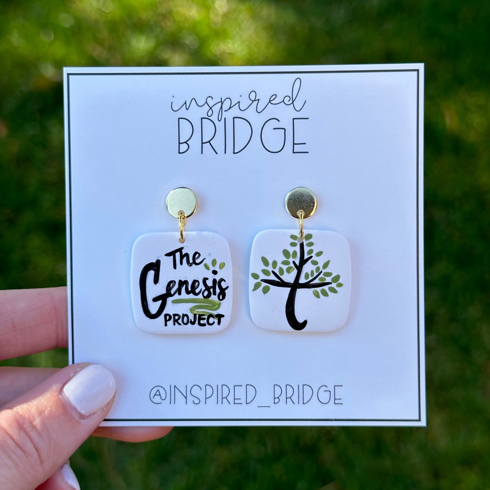 Hand-painted earrings featuring the Genesis Project name and logo. 